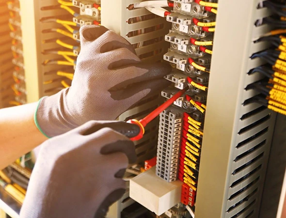 Technician in safety gloves using screwdriver for expert electrical service during lighting system upgrade.