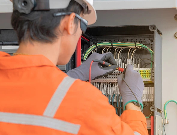 Technician in uniform testing a circuit board during professional outlet and switch repair service for safe operation.