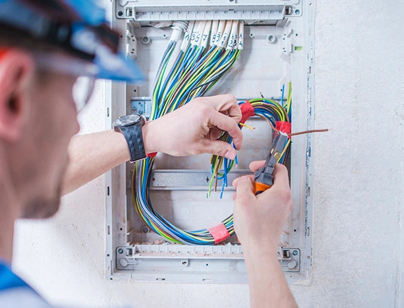 Electrician using pliers to work on electric wires inside a junction box, ensuring safe and precise connections.