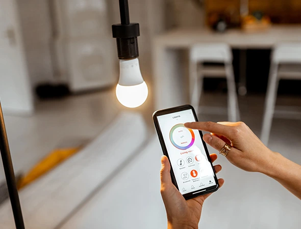 User controlling light bulb color and brightness with a mobile phone in hand for smart home lighting control.